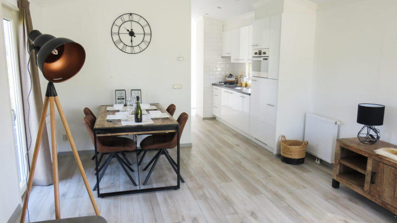 Interior de lodge luminoso con comedor, cocina moderna, lámpara de pie y reloj decorativo de pared.