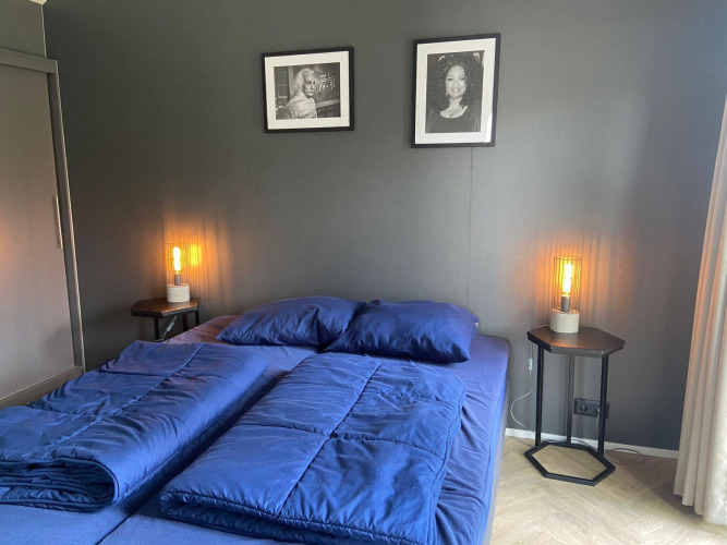 Dormitorio moderno en Velthorst Lodge en Kaatsheuvel con sábanas azules, dos retratos y lámparas laterales cálidas.