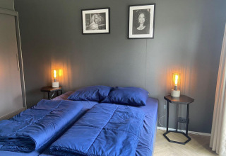 Dormitorio moderno en Velthorst Lodge en Kaatsheuvel con sábanas azules, dos retratos y lámparas laterales cálidas.