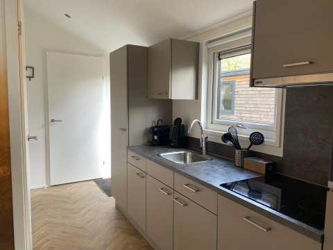 Cucina moderna della lodge Velthorst a Kaatsheuvel, Paesi Bassi, con armadi grigi e finestra.