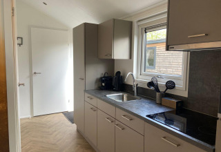 Cucina moderna della lodge Velthorst a Kaatsheuvel, Paesi Bassi, con armadi grigi e finestra.