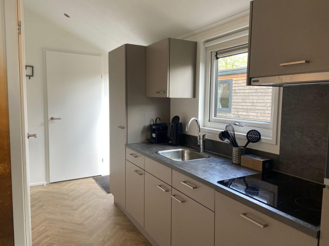 Cocina moderna de la cabaña Velthorst en Kaatsheuvel, Países Bajos, con gabinetes grises y ventana.