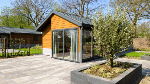 Modernes Chalet Velthorst mit Holzfassade, großen Fenstern und gepflasterter Terrasse mit Pflanzbecken.