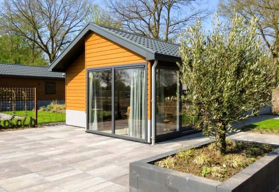 Modernes Chalet Velthorst mit Holzfassade, großen Fenstern und gepflasterter Terrasse mit Pflanzbecken.