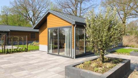 Moderno chalet Velthorst con fachada de madera, grandes ventanales y patio de baldosas con jardineras.