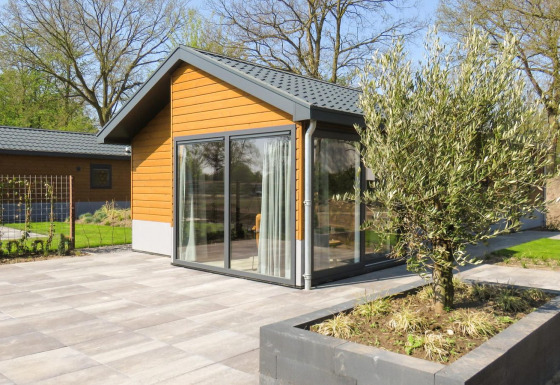 Moderno chalet Velthorst con fachada de madera, grandes ventanales y patio de baldosas con jardineras.