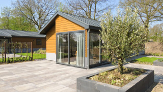Modern Velthorst chalet with wooden facade, large glass doors, tiled patio, and planted garden beds.