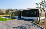 Modern Velthorst chalet in Kaatsheuvel, Netherlands, featuring a gravel driveway, lawn, and young trees.