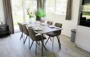 Coin repas lumineux et moderne au glamping Velthorst avec table dressée pour six personnes, grandes fenêtres.