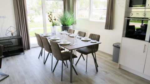 Coin repas lumineux et moderne au glamping Velthorst avec table dressée pour six personnes, grandes fenêtres.
