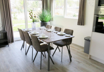 Comedor luminoso y moderno en Velthorst glamping con mesa puesta para seis personas y grandes ventanales.