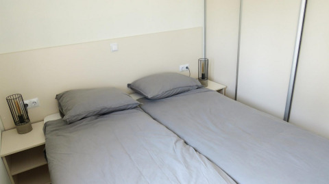 Two single beds with grey bedding in a Velthorst glamping accommodation, nightstands and modern lamps.