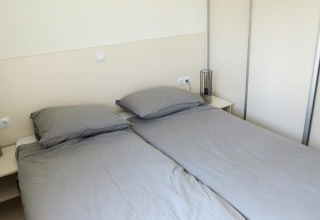 Deux lits simples avec des draps gris dans un hébergement glamping Velthorst, tables de nuit et lampes.