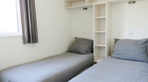 Interior view of a Velthorst glamping accommodation featuring two single beds with grey bedding.