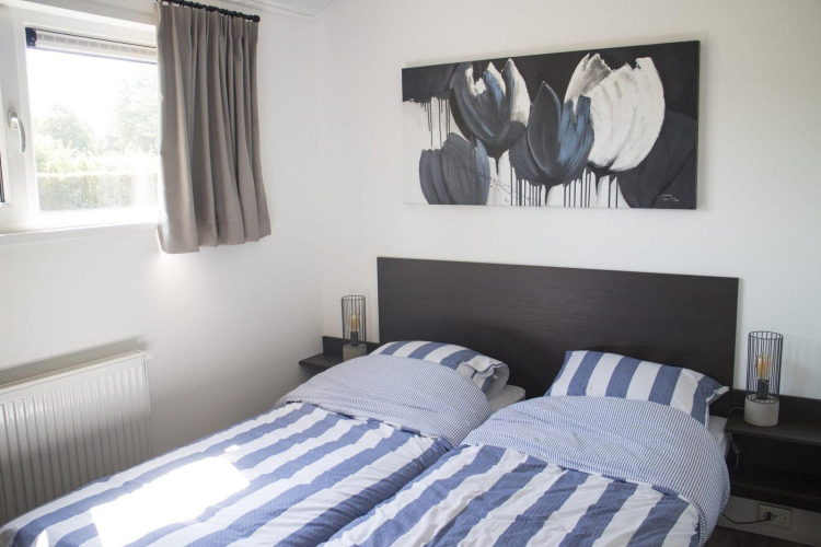 Dos camas individuales con sábanas a rayas azules y blancas en una habitación luminosa de glamping Velthorst.