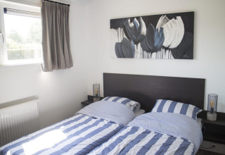 Dos camas individuales con sábanas a rayas azules y blancas en una habitación luminosa de glamping Velthorst.