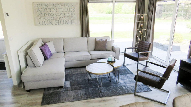 Sala moderna y luminosa en el chalet Velthorst en Kaatsheuvel, Países Bajos, con ventanales y sofá esquinero.