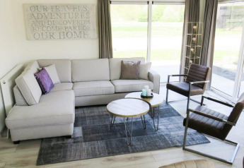 Sala moderna y luminosa en el chalet Velthorst en Kaatsheuvel, Países Bajos, con ventanales y sofá esquinero.