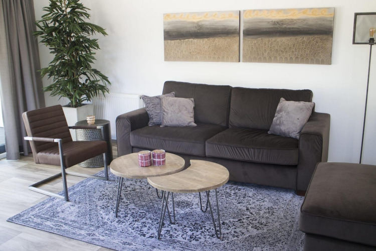 Sala moderna en chalet Velthorst en Kaatsheuvel, Países Bajos, con sofá, sillón, mesas y decoración.