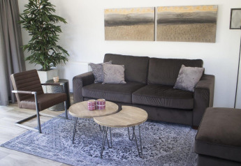 Sala moderna en chalet Velthorst en Kaatsheuvel, Países Bajos, con sofá, sillón, mesas y decoración.