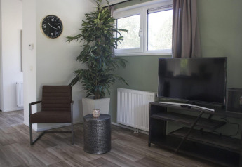 Sala moderna en Chalet Velthorst, Kaatsheuvel, Países Bajos, con sillón, televisión, reloj y planta.