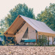 En moderne glamping-safariteltsplads i solskin med cykler, havemøbler og grønne træer i baggrunden.