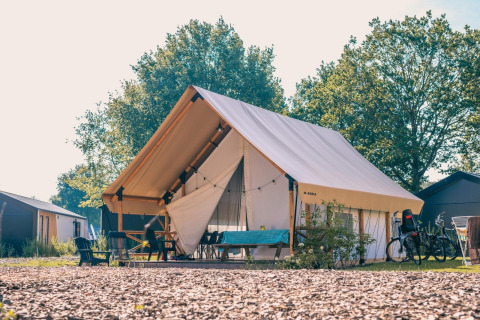 Tenda safari glamping moderna in campeggio soleggiato, con posti a sedere, biciclette e alberi verdi.