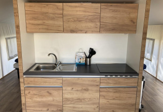 Modern kitchenette inside a glamping tent in Kaatsheuvel, Netherlands, with wood cabinets and stovetop.