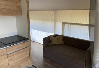 Zona interior de una tienda glamping en Kaatsheuvel, Países Bajos, con sofá, cocina y luz natural.