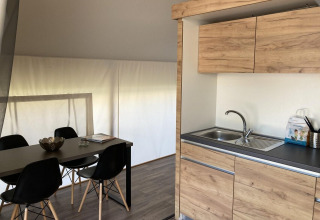 Interior of a glamping tent featuring a modern kitchen and dining table with black chairs in Kaatsheuvel.