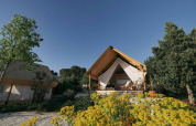 Glamping-Zelt in Kaatsheuvel, Niederlande, umgeben von Blumen, Bäumen und klarem blauen Himmel.