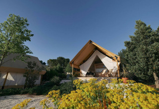 Tienda glamping en Kaatsheuvel, Países Bajos, rodeada de flores, árboles y un cielo azul despejado.