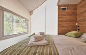 Cama confortable con cojines verdes en una tienda glamping en Kaatsheuvel, Países Bajos, con vista exterior.