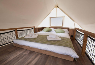 Interno di una tenda glamping con letto matrimoniale, cuscini verdi e asciugamani a Kaatsheuvel, Paesi Bassi.