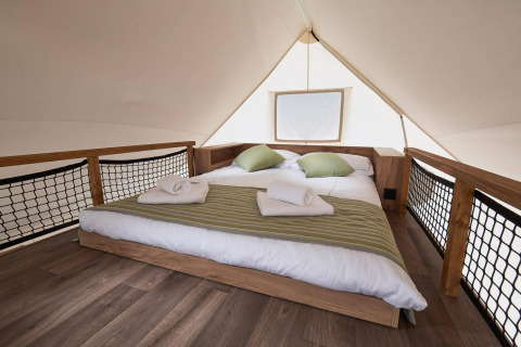 Interior de una tienda glamping en Kaatsheuvel, Países Bajos, con cama doble, cojines verdes y suelo de madera.