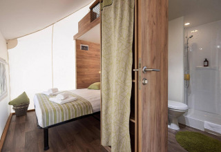 Habitación de lodge luminosa con cama doble, detalles verdes y baño privado con ducha y decoración moderna.