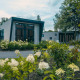 Moderne lodge Just Nature omgivet af frodige haver og blomster, med store vinduer og naturligt lys.