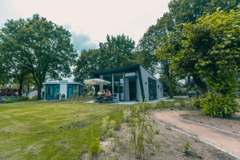 Lodge moderne Just Nature à Kaatsheuvel aux Pays-Bas, avec des personnes dînant dehors entourées d’arbres verts.