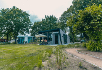 En moderne hytte Just Nature i Kaatsheuvel, Holland, med folk der sidder udendørs omgivet af grønne træer.