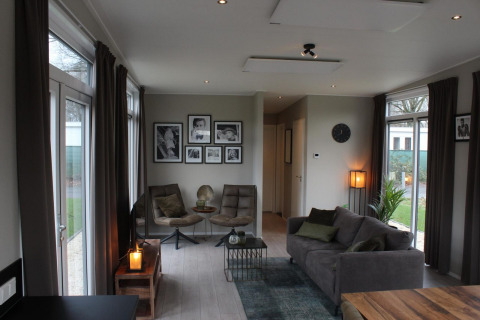 Sala moderna en Just Nature lodge en Kaatsheuvel, Países Bajos, con sofá, sillas y cuadros en la pared.