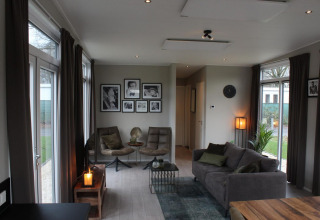 Sala moderna en Just Nature lodge en Kaatsheuvel, Países Bajos, con sofá, sillas y cuadros en la pared.