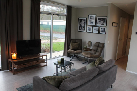 Modernes Wohnzimmer in der Just Nature Lodge in Kaatsheuvel, Niederlande, mit Sofa, TV und Fensterblick.