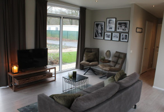 Modernes Wohnzimmer in der Just Nature Lodge in Kaatsheuvel, Niederlande, mit Sofa, TV und Fensterblick.