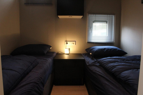 Dos camas individuales con ropa de cama oscura en una pequeña habitación de Just Nature en Kaatsheuvel, Países Bajos.