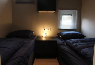 Deux lits simples avec une literie foncée dans une petite chambre du lodge Just Nature à Kaatsheuvel, Pays-Bas.