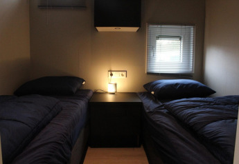 Deux lits simples avec une literie foncée dans une petite chambre du lodge Just Nature à Kaatsheuvel, Pays-Bas.