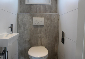 Baño moderno con inodoro, lavabo pequeño y pared gris en Just Nature lodge en Kaatsheuvel, Países Bajos.