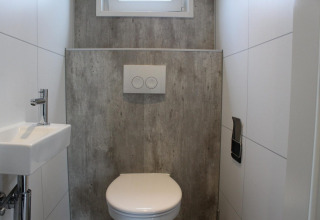 Bagno moderno con wc, piccolo lavandino e parete grigia al lodge Just Nature a Kaatsheuvel, Paesi Bassi.