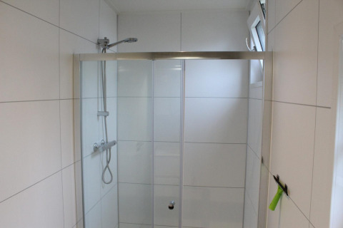 Ducha moderna con puertas de vidrio y azulejos blancos en el lodge Just Nature en Kaatsheuvel, Países Bajos.