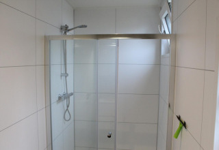 Box doccia moderno con porte in vetro e piastrelle bianche presso Just Nature lodge a Kaatsheuvel, Paesi Bassi.